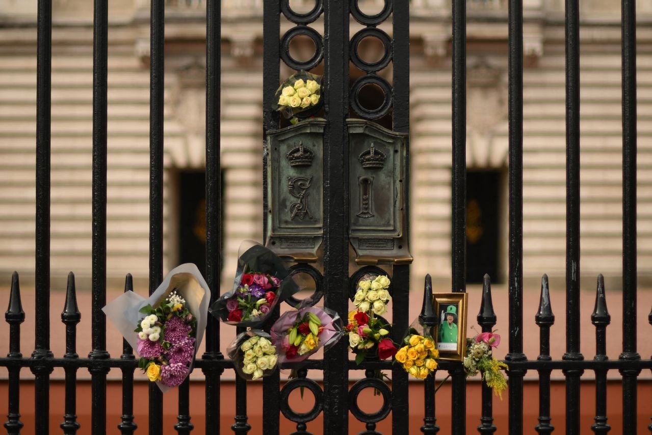 Una fotografía enmarcada de la reina Isabel II de Gran Bretaña y tributos florales se ven en las rejas del Palacio de Buckingham en el centro de Londres el 8 de septiembre de 2023, mientras los simpatizantes conmemoran la vida de Su difunta Majestad la Reina Isabel II en el primer aniversario de su fallecimiento. (Foto de Daniel LEAL / AFP)