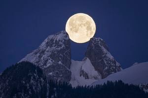 La luna llena se pone detrás de las montañas, incluidos los picos gemelos de Les Jumelles en Chablais Valaisan, cerca de Aigle, Suiza, el lunes 6 de febrero de 2023. 