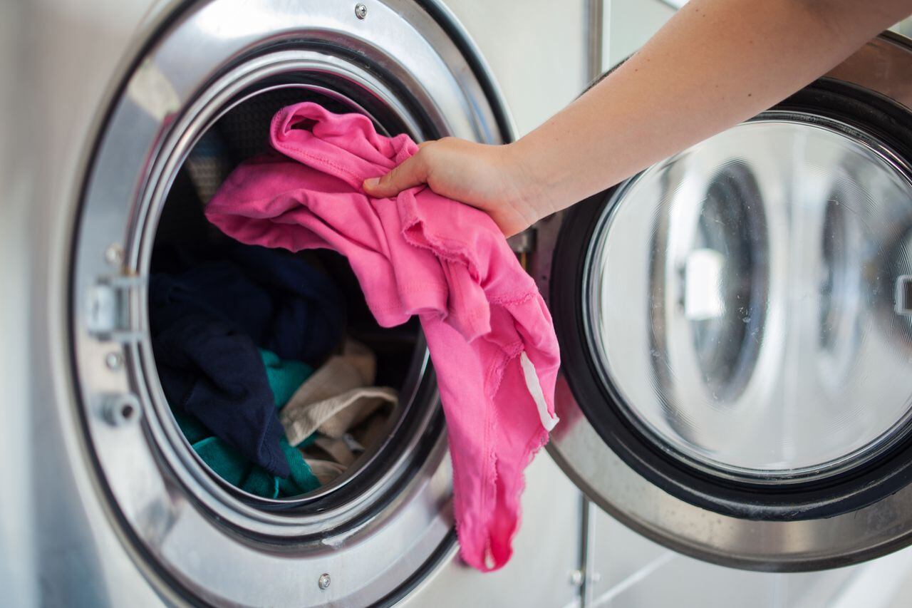 Woman putting pink shirt into washing machine.