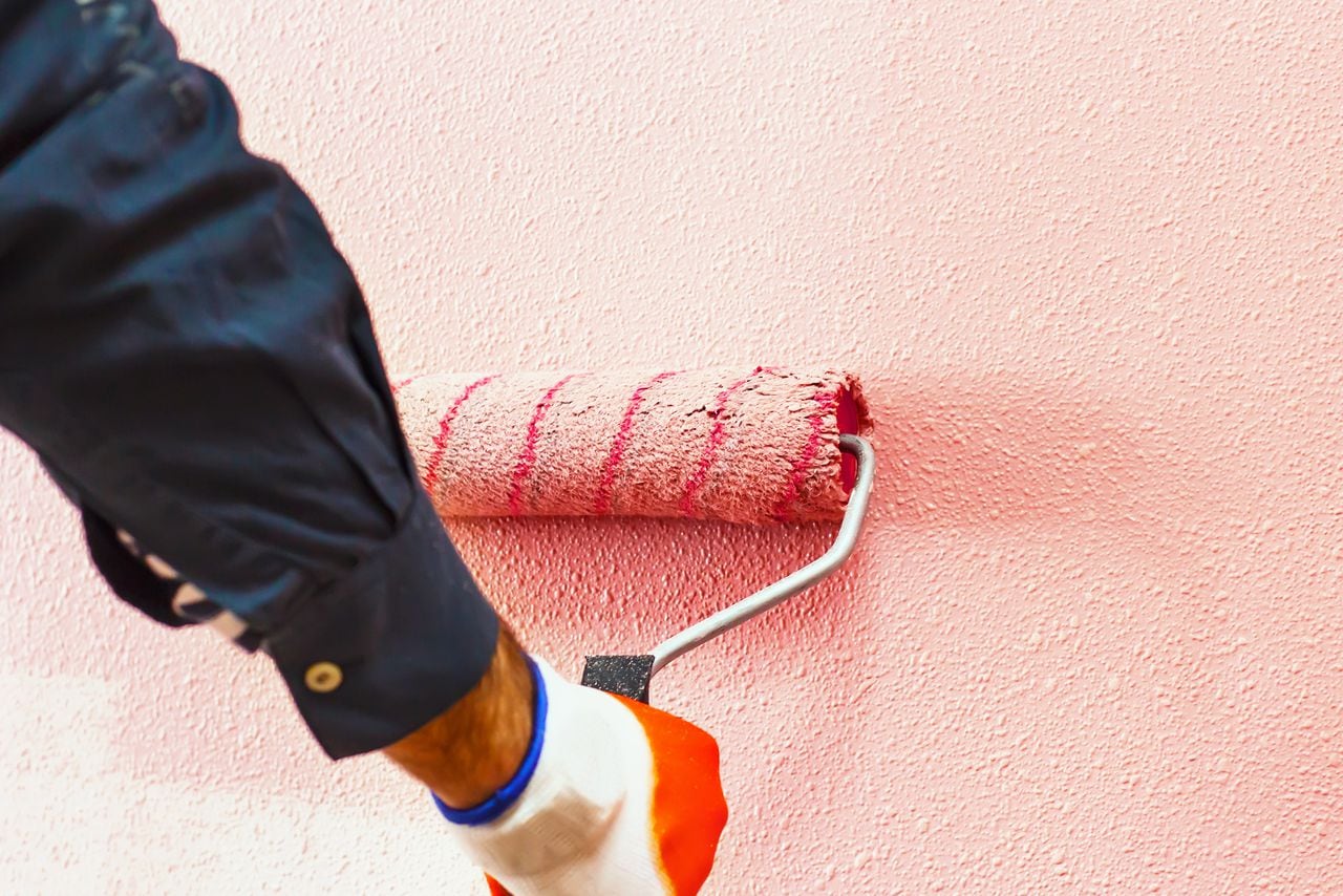 Hombre pinta la pared a mano con un rodillo de pintura mientras se trabaja en interiores, hacer reparaciones