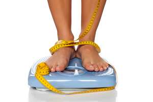 Pies de mujer en una báscula doméstica y cinta métrica alrededor de ellos.