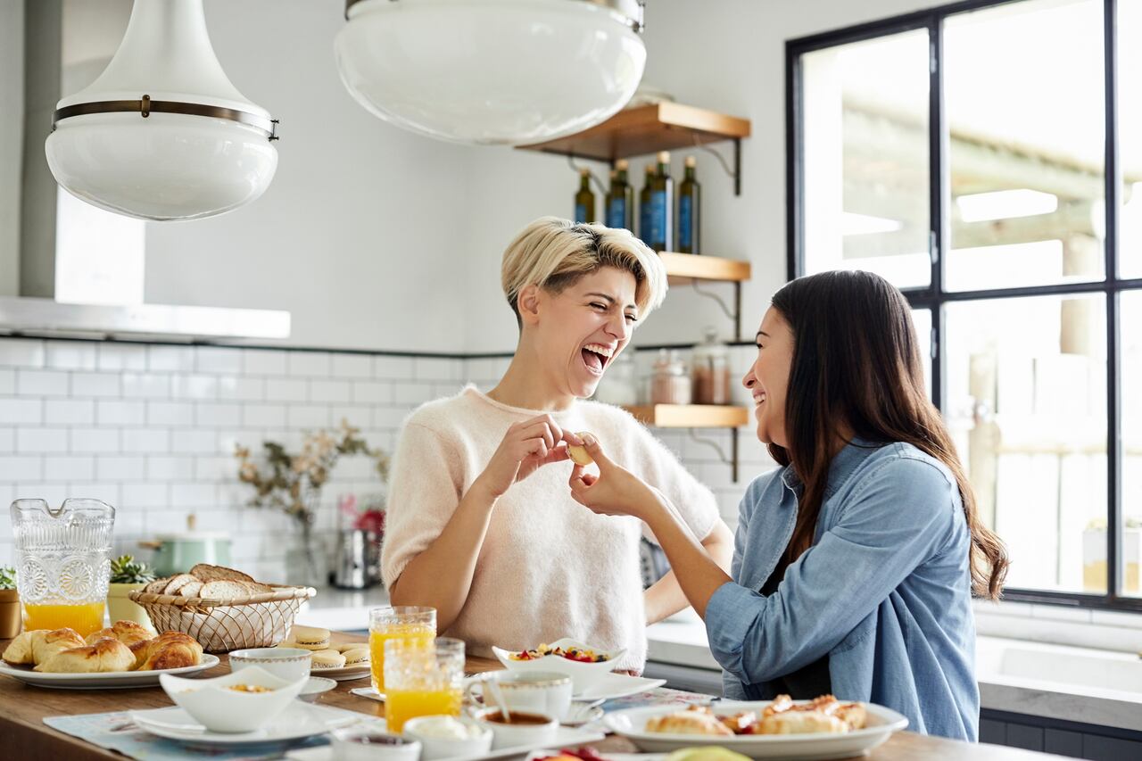 Happy young women having breakfast together. Female couple is spending leisure time at home. They are in kitchen.