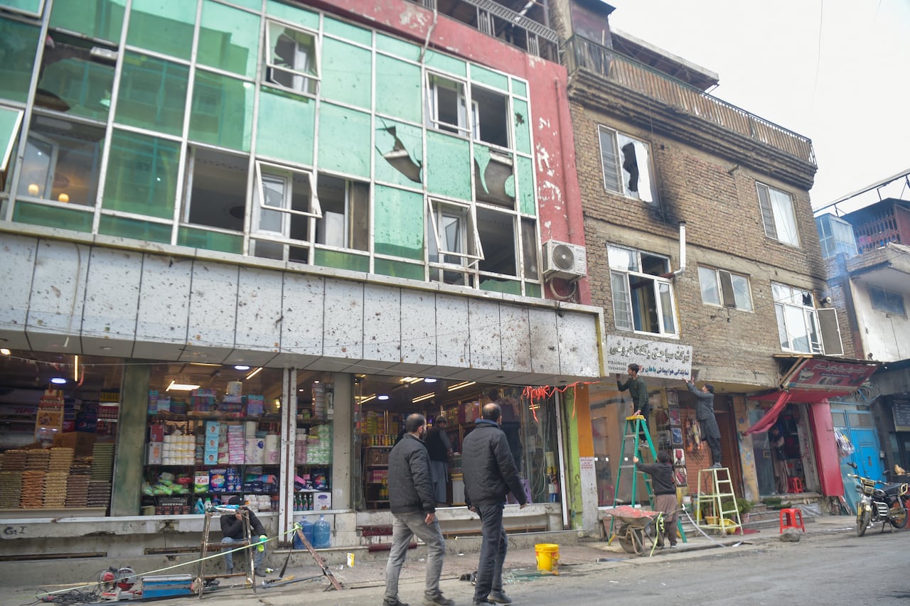 Locals walk past shattered glass of a building, following an explosion in the Shahr-e Naw area of Kabul on January 20, 2026. Mourners gathered on January 20 for the funeral of a Chinese man killed in a restaurant bombing in central Kabul, where Afghans were picking up the pieces of their shattered shops. (Photo by Bais YUSUFI / AFP)