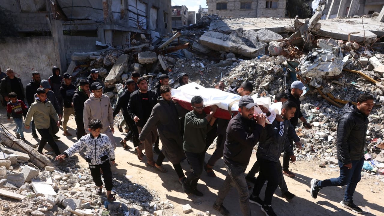 Hombres palestinos cargan el cuerpo de una persona fallecida en un ataque militar israelí, mientras maniobran entre los escombros de un edificio destruido por el ejército israelí, durante su funeral en Khan Yunis, en el sur de la Franja de Gaza, el 27 de febrero de 2026. El Ministerio de Defensa Civil de Gaza declaró que los ataques israelíes mataron al menos a cinco personas el 27 de febrero de 2026.