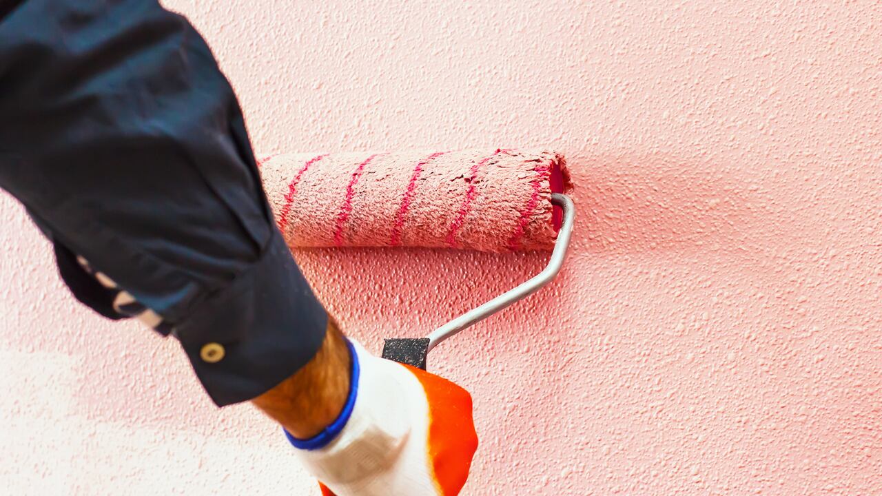 Hombre pinta la pared a mano con un rodillo de pintura mientras se trabaja en interiores, hacer reparaciones