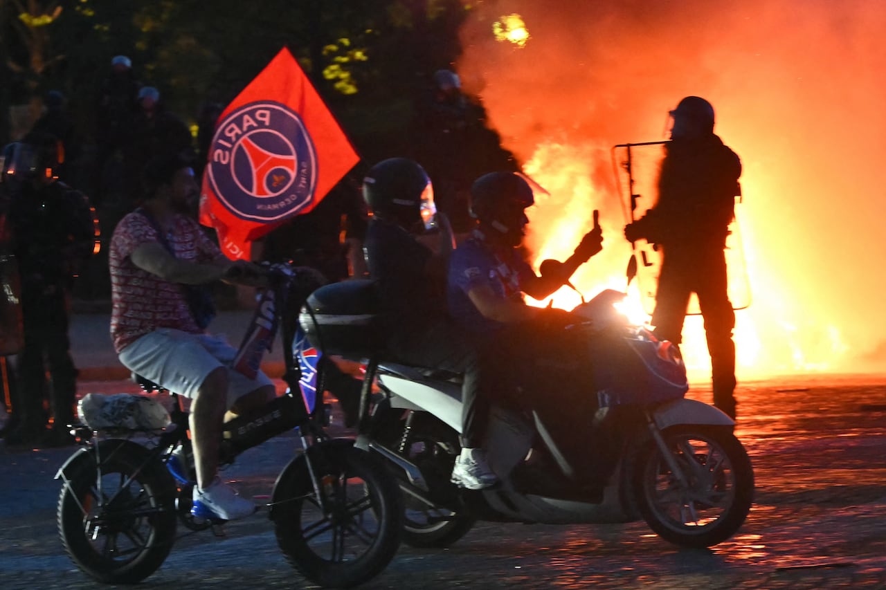 Aficionados del PSG pasan en sus patinetes eléctricos junto a agentes antidisturbios (al fondo a la derecha) mientras celebran la victoria de su equipo en la final de la Liga de Campeones de la UEFA entre el Paris Saint-Germain (PSG) y el Arsenal FC, disputada en Budapest, en la Plaza del Trocadero de París el 30 de mayo de 2026. (Foto de LOU BENOIST / AFP)