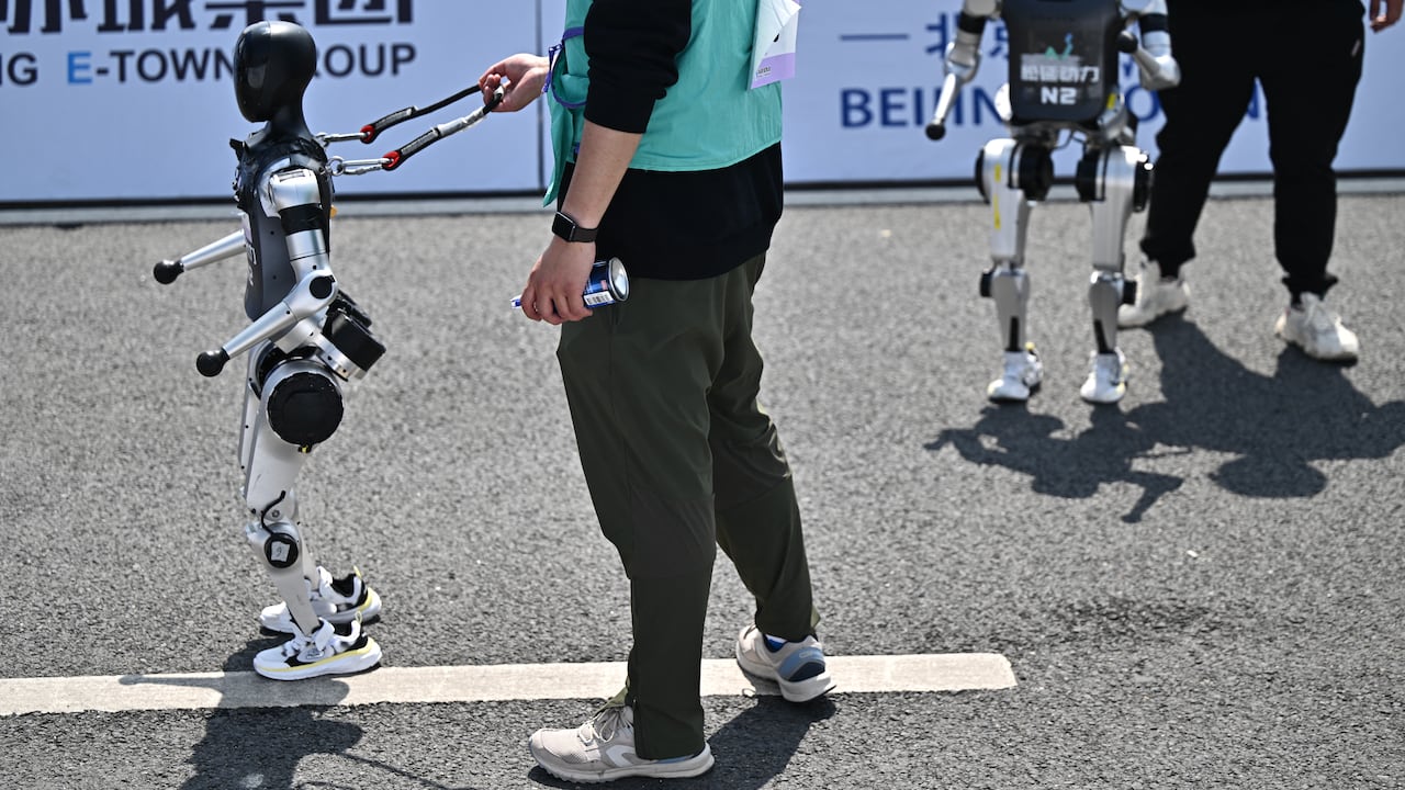 Se ve a robots y sus ingenieros tras cruzar la meta en la media maratón de robots humanoides celebrada en Pekín el 19 de abril de 2025. Decenas de robots humanoides recorrieron las calles de Pekín, uniéndose a miles de sus homólogos de carne y hueso en una media maratón pionera a nivel mundial que demostró el impulso de China por liderar la carrera global en tecnología de vanguardia. (Foto de Pedro PARDO / AFP)