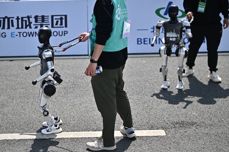 Se ve a robots y sus ingenieros tras cruzar la meta en la media maratón de robots humanoides celebrada en Pekín el 19 de abril de 2025. Decenas de robots humanoides recorrieron las calles de Pekín, uniéndose a miles de sus homólogos de carne y hueso en una media maratón pionera a nivel mundial que demostró el impulso de China por liderar la carrera global en tecnología de vanguardia. (Foto de Pedro PARDO / AFP)