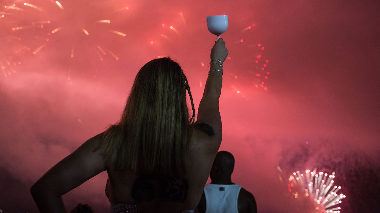 La gente celebra mientras los tradicionales fuegos artificiales de Año Nuevo iluminan el cielo en la playa de Copacabana.