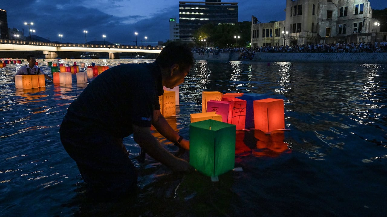 Voluntarios (izq.) empujan linternas de papel hacia el río Motoyasu, pasando por la cúpula de la bomba atómica (detrás), después de que fueron liberadas por visitantes para conmemorar el 80.º aniversario del primer ataque con bomba atómica del mundo, en la ciudad de Hiroshima el 6 de agosto de 2025. (Foto de Richard A. Brooks / AFP)
