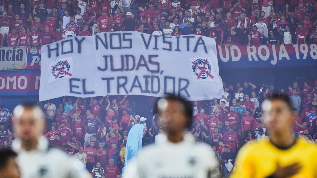 Juan Guillermo Cuadrado (centro) y atrás la pancarta o trapo de los hinchas del Independiente Medellín en su contra.