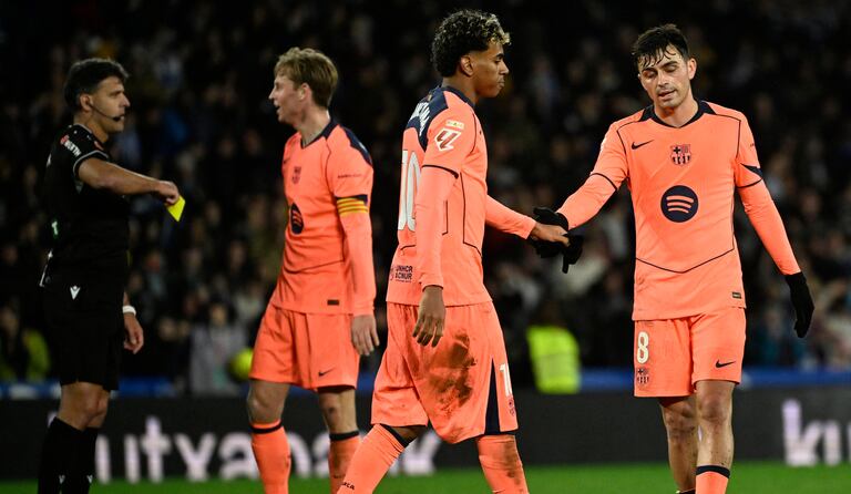 El centrocampista español #08 del Barcelona, Pedri, y el delantero español #10 del Barcelona, Lamine Yamal (2D), se dan la mano mientras el árbitro español Jesús Gil (I) muestra una tarjeta amarilla al delantero holandés #26 del FC Porto, Luuk De Jong, durante el partido de fútbol de la liga española entre la Real Sociedad y el FC Barcelona en el Estadio de Anoeta en San Sebastián el 18 de enero de 2026. (Foto de ANDER GILLENEA / AFP)