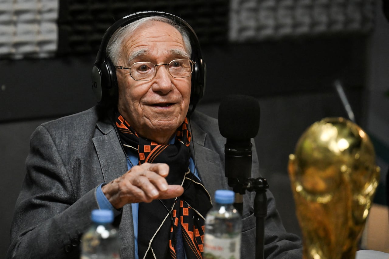 El periodista deportivo y analista de fútbol argentino Enrique Macaya Márquez, de 91 años, participa en una transmisión en vivo de DSports Radio en Munro, provincia de Buenos Aires, Argentina, el 29 de mayo de 2026, junto a una réplica del trofeo de la Copa Mundial de la FIFA. Desde Suecia 1958, el fútbol ha cambiado en términos tácticos, tecnológicos y económicos. Sin embargo, algo se ha mantenido constante: la presencia del periodista argentino Enrique Macaya Márquez, quien extenderá su récord de cobertura de Copas Mundiales a 18 en Norteamérica 2026. (Foto de Luis ROBAYO / AFP)