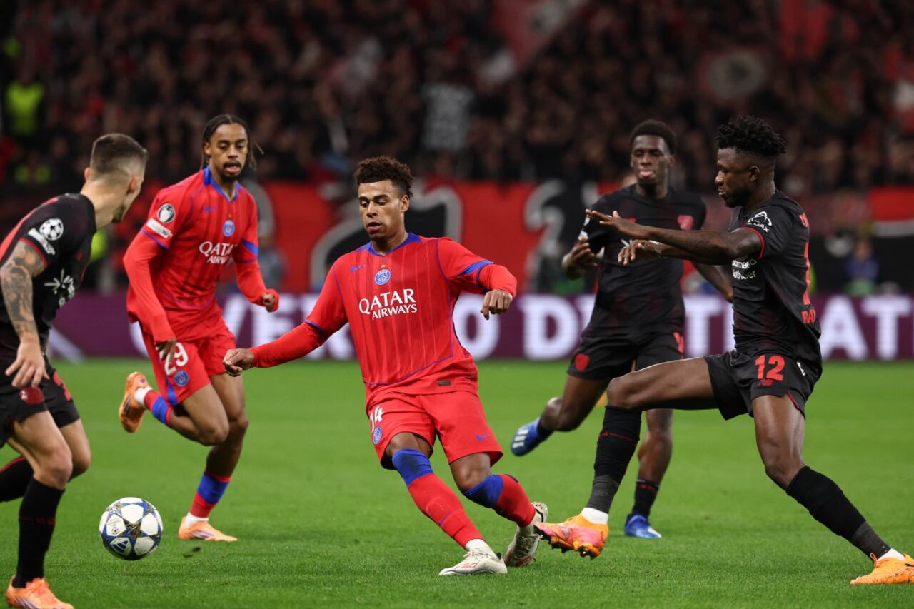 El centrocampista francés #14 del Paris Saint-Germain, Desire Doue (C), y el defensa burkinés #12 del Bayer Leverkusen, Edmond Tapsoba (R), compiten por el balón durante el partido de fútbol de la UEFA Champions.
