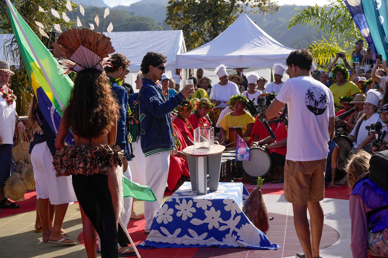 El brasileño Gabriel Medina levanta un vaso de arena de una playa de Brasil para agregarlo a una embarcación durante la ceremonia de apertura de la competencia de surf de los Juegos Olímpicos de Verano de 2024, el viernes 26 de julio de 2024, en Papara, Tahití. (Foto AP/Gregory Bull)