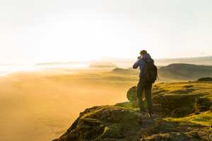 Un hombre tomando fotos de la puesta de sol desde lo alto de un acantilado en Islandia.