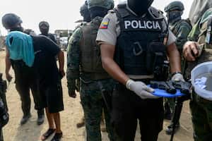 Un policía muestra armas incautadas junto a un hombre detenido durante un operativo conjunto entre la policía nacional y las fuerzas armadas en el barrio "Una Sola Fuerza" en Durán, Ecuador, el 16 de octubre de 2024. (Foto de Gerardo MENOSCAL / AFP)