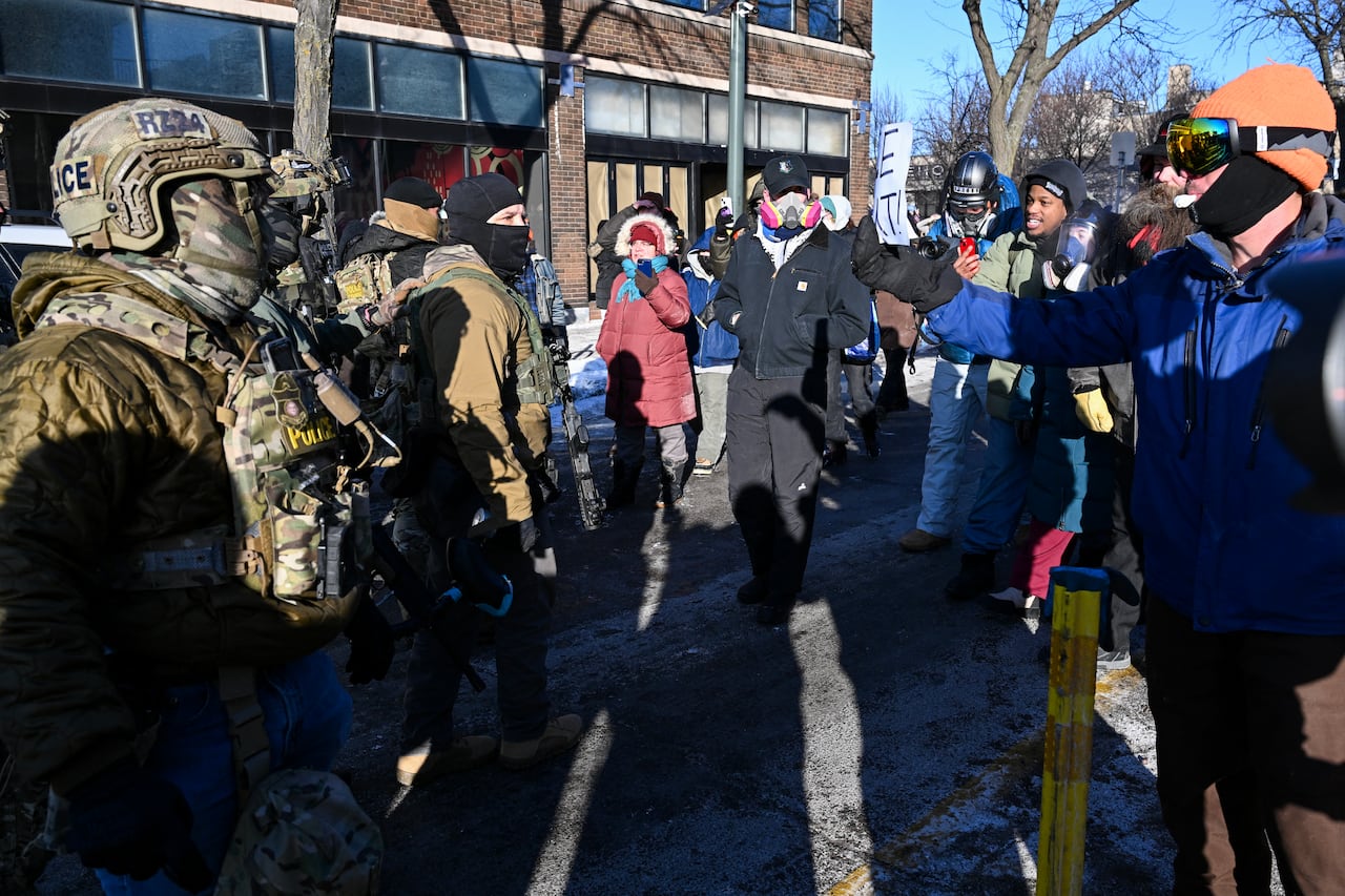 Federal agents (L) look on as demonstators gather near the site of where state and local authorities say a man was shot by federal agents earlier in the morning in Minneapolis, Minnesota, on January 24, 2026. Minnesota Governor Tim Walz said Saturday that federal agents deployed in Minneapolis as part of a sweeping immigration crackdown had carried out "another horrific shooting," less than three weeks after the fatal shooting of Renee Good. (Photo by ROBERTO SCHMIDT / AFP)