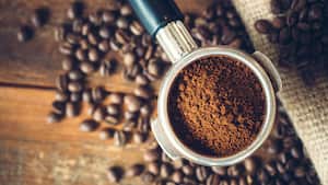 Espresso recién molido en un portafiltro, listo para convertirse en un espresso caliente. Fondo de madera rústica, una bolsa de café de arpillera en el fondo cubierta con granos de café tostados. Vista aérea.