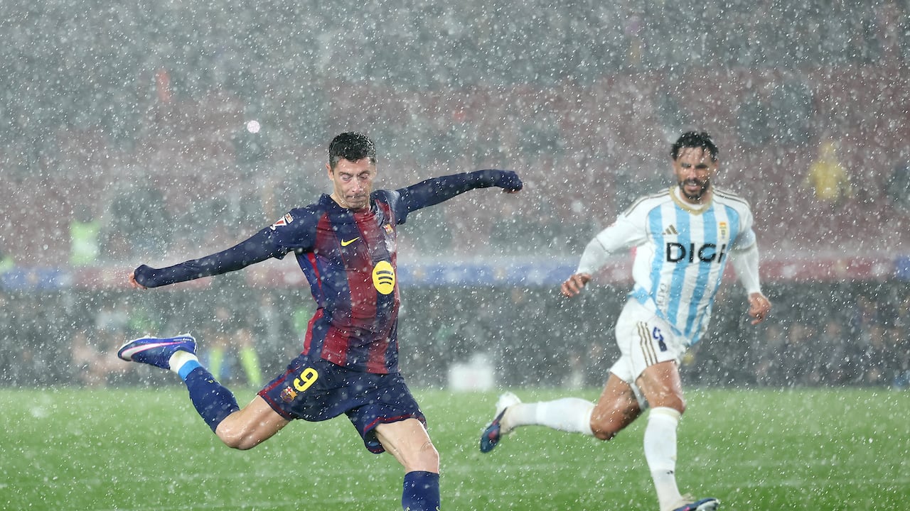 El delantero polaco #09 del Barcelona, Robert Lewandowski (izq.), dispara bajo una fuerte tormenta de granizo durante el partido de la liga española entre el FC Barcelona y el Real Oviedo en el estadio Camp Nou de Barcelona el 25 de enero de 2026. (Foto de Josep LAGO / AFP)