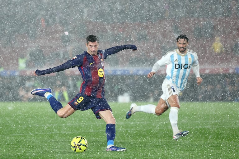 El delantero polaco #09 del Barcelona, Robert Lewandowski (izq.), dispara bajo una fuerte tormenta de granizo durante el partido de la liga española entre el FC Barcelona y el Real Oviedo en el estadio Camp Nou de Barcelona el 25 de enero de 2026. (Foto de Josep LAGO / AFP)