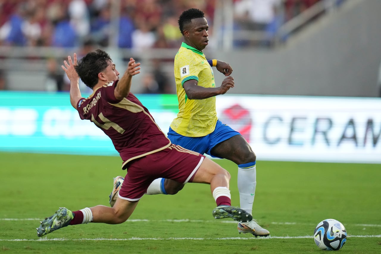 El brasileño Vinicius Junior, derecha, regatea al venezolano Jon Aramburu durante un partido de fútbol de clasificación para la Copa Mundial de la FIFA 2026 en el estadio Monumental de Maturín, Venezuela, el jueves 14 de noviembre de 2024. (Foto AP/Ariana Cubillos)