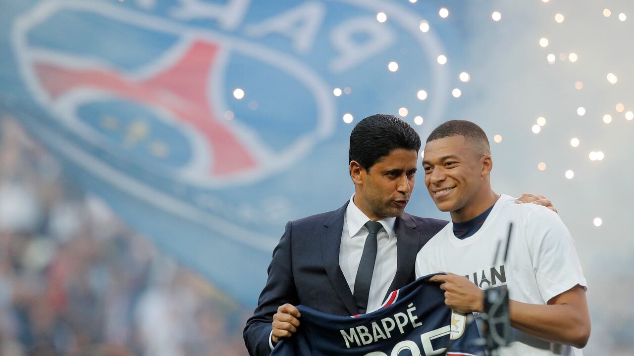 PSG President Nasser Al-Khelaifi, left, speaks to PSG's Kylian Mbappe who holds a shirt with his name and 2025 on it as it is announced he has signed a three year extension to his contract on the pitch ahead of the French League One soccer match between Paris Saint Germain and Metz at the Parc des Princes stadium in Paris, France, Saturday, May 21, 2022. (AP Photo/Michel Spingler)