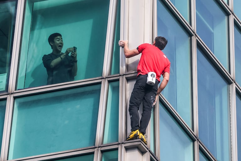 Un ocupante del edificio graba con su teléfono al escalador estadounidense Alex Honnold mientras escala el edificio Taipei 101 sin cuerdas ni equipo de seguridad en Taipéi el 25 de enero de 2026. (Foto de I-Hwa Cheng / AFP)