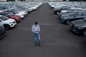 Latin American salesman using a tablet while being surrounded by cars at the dealership