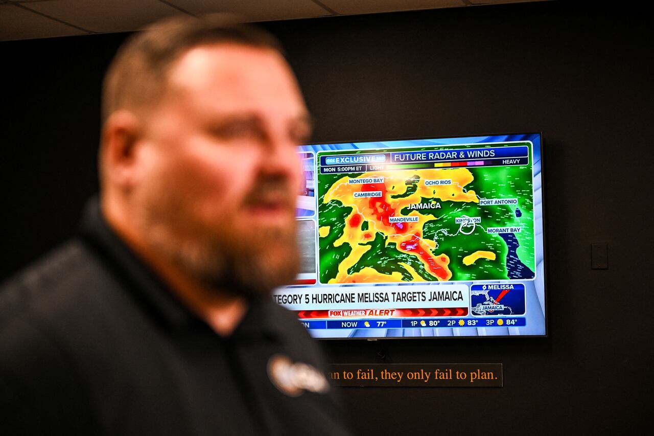 Un canal de noticias meteorológicas muestra actualizaciones sobre el huracán Melissa mientras Billy Richardson, director de almacenamiento estadounidense de Global Empowerment Mission, habla durante una entrevista con la AFP