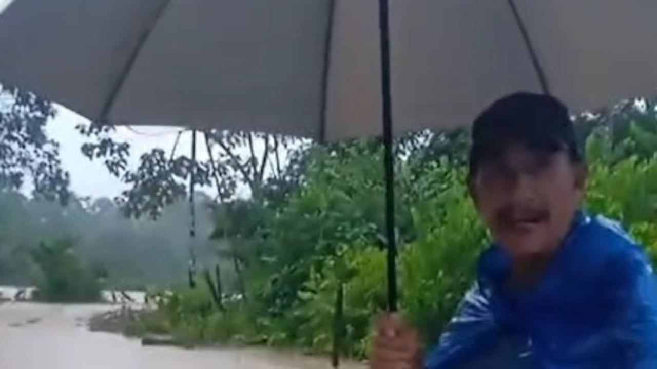 El campesino de este municipio, con sombrilla en mano, con botas pantaneras y en medio del agua, informa a los profesores de su hija que no puede ir a clases por el desbordamiento del río Tambor.