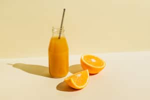 Botella colorida de jugo de naranja recién exprimido con ingredientes frescos naranjas sobre fondo beige. Superalimentos, alimentos saludables, bebidas, dieta y concepto de desintoxicación. Plano, vista superior, espacio de copia
