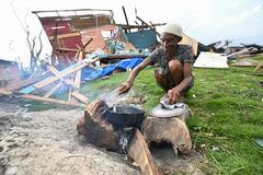 Dorothy Headley, de 75 años, prepara una comida de hígado de vaca sobre un fuego de leña mientras se ven propiedades dañadas al fondo tras el paso del huracán Melissa en la comunidad de Watercress, Westmoreland, Jamaica, el 31 de octubre de 2025.