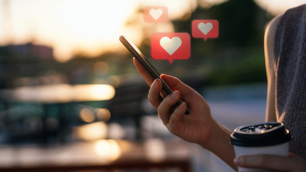 Primer plano de una joven que revisa la red social en un teléfono inteligente mientras viaja por la ciudad. Teléfono móvil con mensaje de burbuja de discurso emoji de corazón en la pantalla.