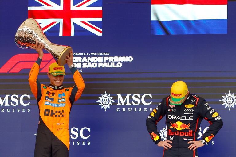 El piloto británico Lando Norris (izq.), ganador del equipo McLaren, levanta el trofeo en el podio pasando junto al piloto holandés Max Verstappen (der.), de Red Bull Racing, que quedó en tercer lugar.