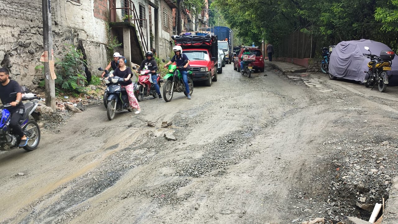Vehículos y peatones enfrentan dificultades para transitar por la vía inundada y convertida en lodazal durante las lluvias.