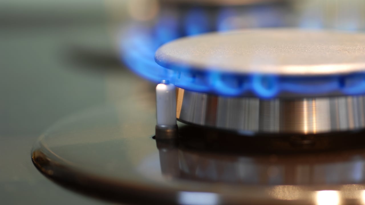 Imagen macro de encimera de gas en plena llama. Concéntrese en el frente del quemador y el encendedor a la izquierda de la llama.