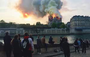 (ARCHIVOS) Los transeúntes observan las llamas y el humo que se elevan desde el techo de la Catedral de Notre-Dame en París el 15 de abril de 2019.
