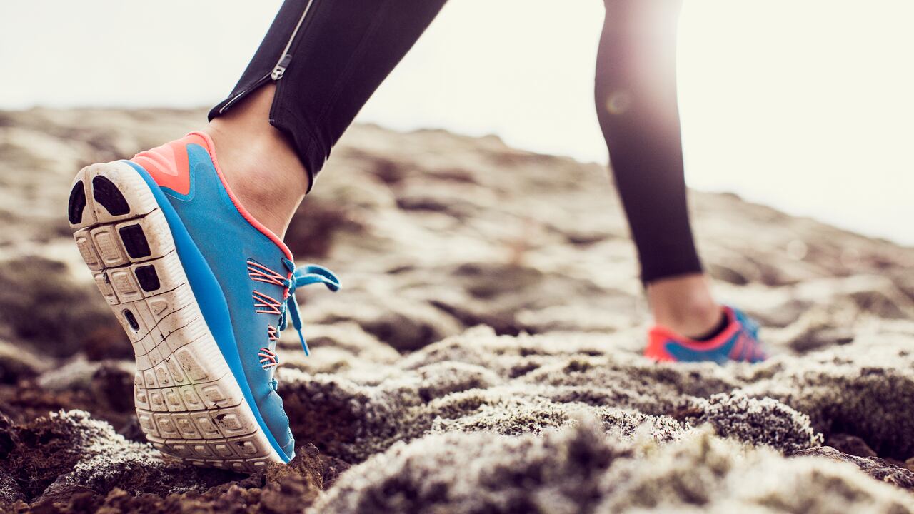 Close up, low angle shot of a female runners trainers, running through mossy terrain in Iceland. Blue trainers, black running leggings with backlit sunshine.