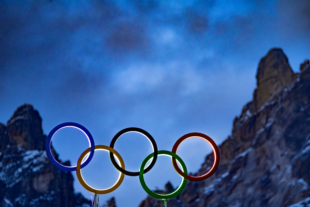 Los anillos olímpicos iluminados se ven en el techo del estadio olímpico con picos de montañas detrás en Cortina d'Ampezzo, norte de Italia, antes de los Juegos Olímpicos de Milán Cortina 2026, el 2 de febrero de 2026. (Foto de Odd ANDERSEN / AFP)
