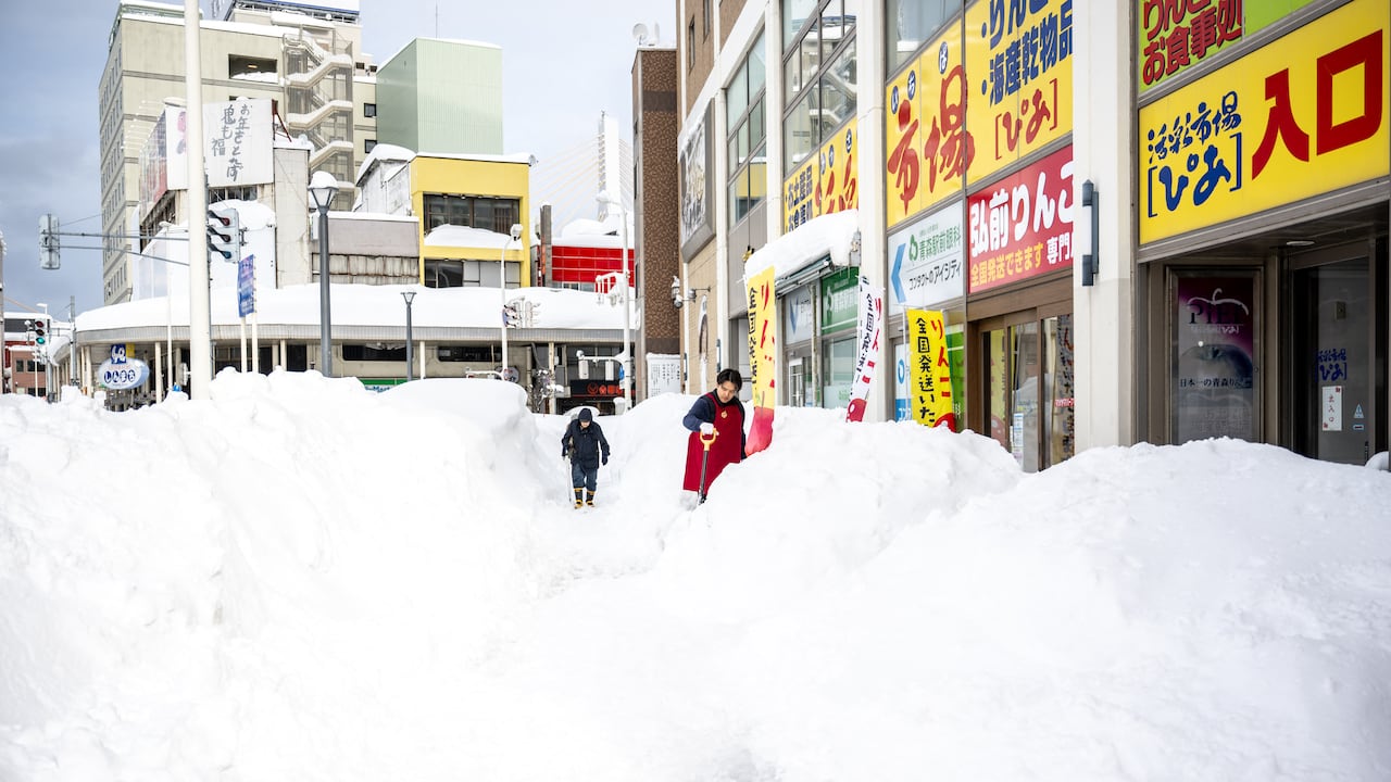 A shop employee (R) shovels the snow in front of the shop in Aomori city, Aomori prefecture on January 30, 2026. (Photo by Philip FONG / AFP)