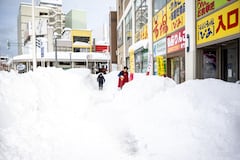 A shop employee (R) shovels the snow in front of the shop in Aomori city, Aomori prefecture on January 30, 2026. (Photo by Philip FONG / AFP)