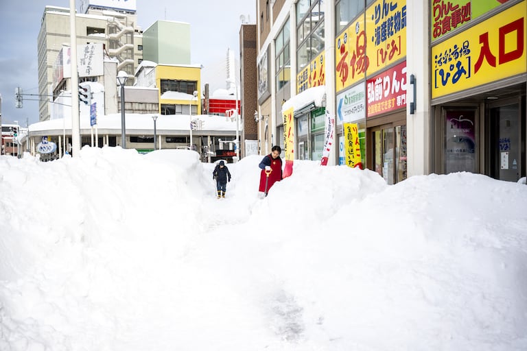 A shop employee (R) shovels the snow in front of the shop in Aomori city, Aomori prefecture on January 30, 2026. (Photo by Philip FONG / AFP)