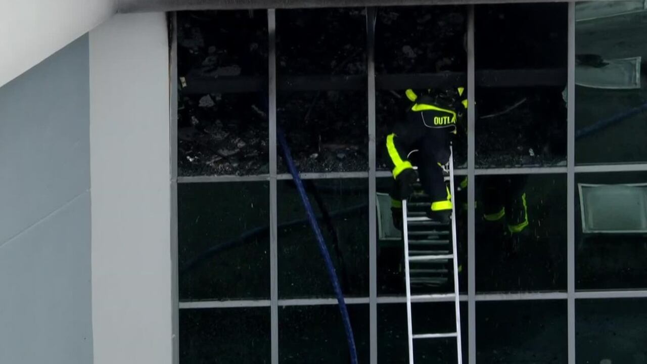 Bomberos rociando agua en un edificio en llamas durante el incendio en Tamarac, mientras el humo cubre la escena.