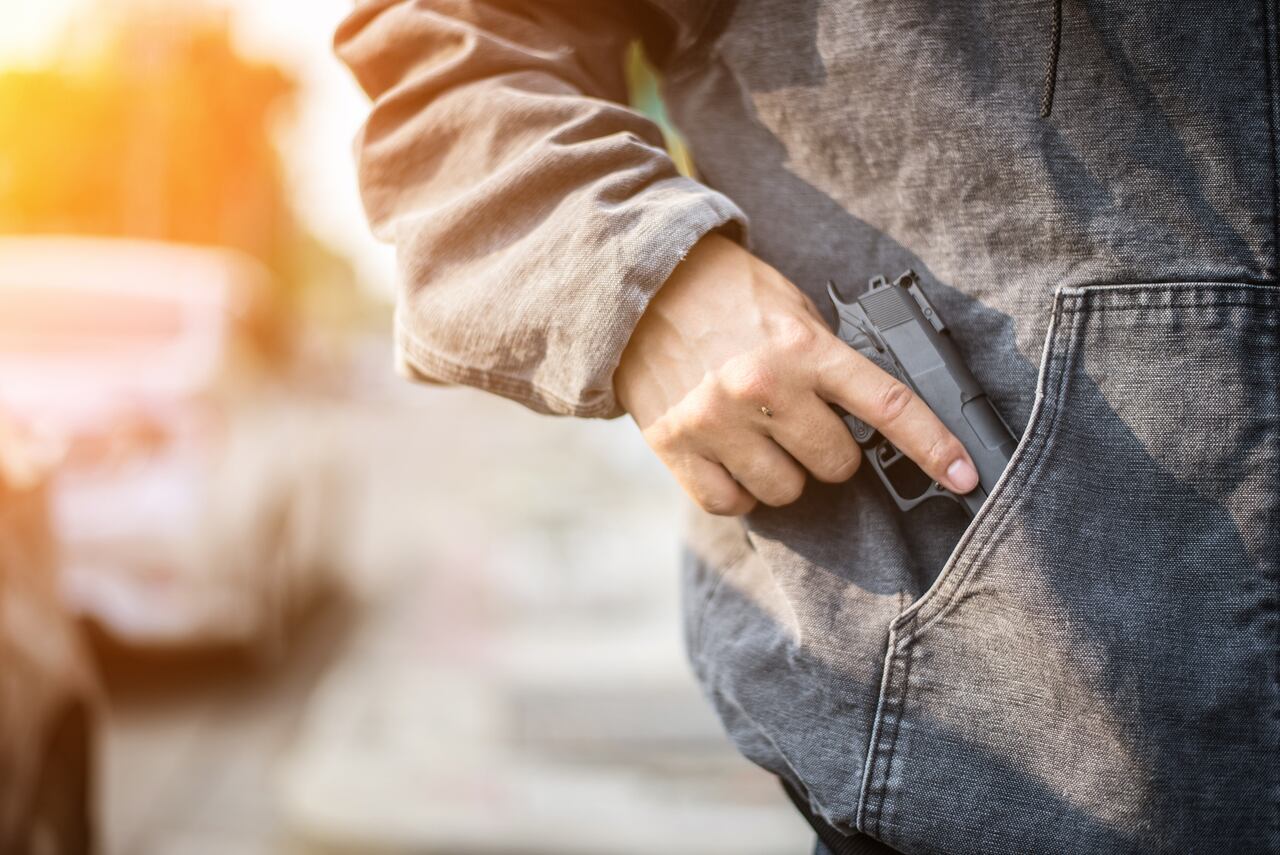 Armed man (attacker) holds pistol in public place. Many people on street. Gun control concept.