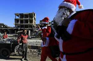 Un niño sirio sonríe mientras los hombres vestidos con trajes de Santa Claus pasan frente a edificios destruidos en la ciudad siria oriental de Raqa el 26 de diciembre de 2017. Foto: AFP / Delil souleiman