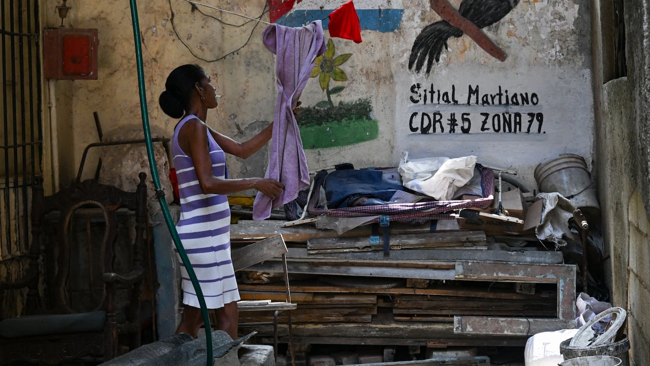 A woman takes a towel from her clothes line in a vacant lot in Havana on May 18, 2026. Cuba's leader warned on May 18 of a "bloodbath" in the event of an American attack, while the US Treasury sanctioned Cuba's main intelligence agency and top leaders as tensions spiked between the arch-foes. (Photo by YAMIL LAGE / AFP)