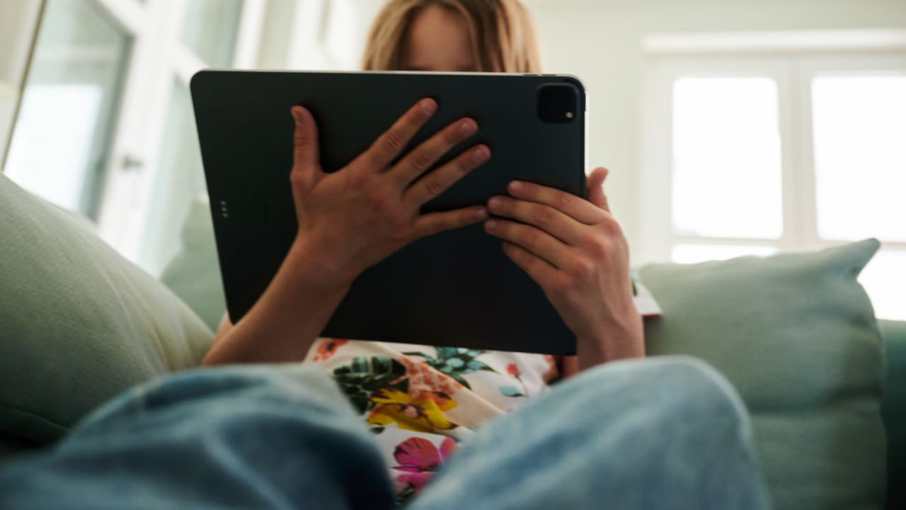 28 de mayo de 2022, Berlín: Una niña se sienta en el sofá y mira la tableta de sus padres. Foto: Annette Riedl/dpa (Foto de Annette Riedl/Picture Alliance vía Getty Images)