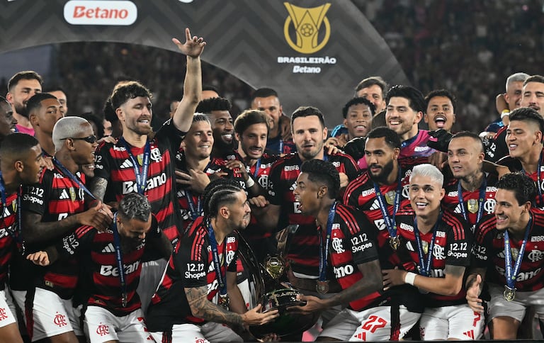 El mediocampista uruguayo del Flamengo #10 Giorgian de Arrascaeta (centro izquierdad) y el delantero #27 Bruno Henrique (centro derecha) levantan el trofeo Brasileirao después de ganar el partido de fútbol Brasileirao Serie A entre Flamengo y Ceará en el estadio Maracaná de Río de Janeiro, Brasil, el 3 de diciembre de 2025. (Foto de Mauro PIMENTEL / AFP)