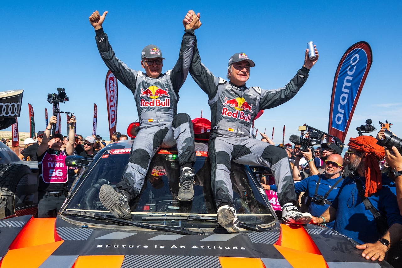 El piloto español del equipo Audi Sport, Carlos Sainz (d), y su copiloto, Lucas Cruzof, celebran su victoria tras cruzar la meta de la etapa 12, de Yanbu a Yanbu, Arabia Saudí, el 19 de enero de 2024, al término del Rally Dakar 2024. El veterano piloto español Carlos Sainz ganó el exigente Rally Dakar por cuarta vez, convirtiéndose a sus 61 años en el ganador de mayor edad de la carrera. (Foto de PATRICK HERTZOG / AFP)